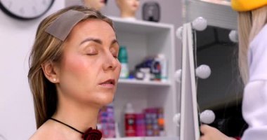 Makyöz, güzellik salonunda genç bir kadının profesyonel makyajını yapıyor.                