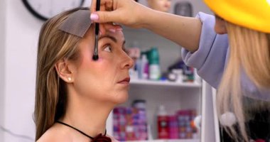 Makyöz, güzellik salonunda genç bir kadının profesyonel makyajını yapıyor.                