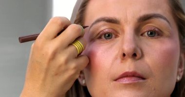 Makyöz, güzellik salonunda genç bir kadının profesyonel makyajını yapıyor.                