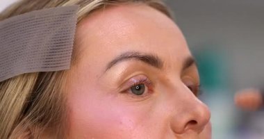 Makyöz, güzellik salonunda genç bir kadının profesyonel makyajını yapıyor.                