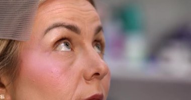 Makyöz, güzellik salonunda genç bir kadının profesyonel makyajını yapıyor.                