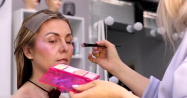 Makyöz, güzellik salonunda genç bir kadının profesyonel makyajını yapıyor.                