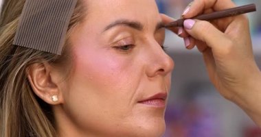 Makyöz, güzellik salonunda genç bir kadının profesyonel makyajını yapıyor.                