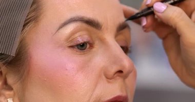Makyöz, güzellik salonunda genç bir kadının profesyonel makyajını yapıyor.                