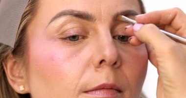 Makyöz, güzellik salonunda genç bir kadının profesyonel makyajını yapıyor.                