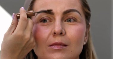 Makyöz, güzellik salonunda genç bir kadının profesyonel makyajını yapıyor.                