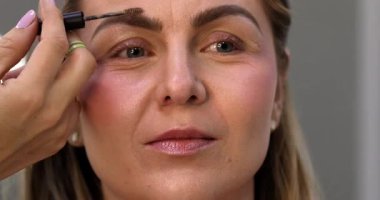 Makyöz, güzellik salonunda genç bir kadının profesyonel makyajını yapıyor.                