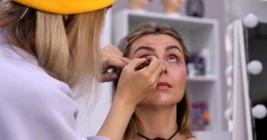 Makyöz, güzellik salonunda genç bir kadının profesyonel makyajını yapıyor.                