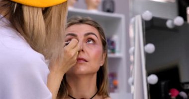 Makyöz, güzellik salonunda genç bir kadının profesyonel makyajını yapıyor.                