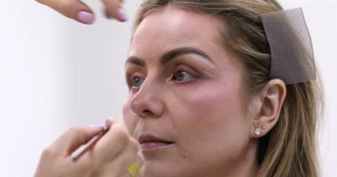 Makyöz, güzellik salonunda genç bir kadının profesyonel makyajını yapıyor.                