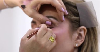 Makyöz, güzellik salonunda genç bir kadının profesyonel makyajını yapıyor.                