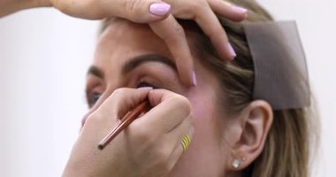 Makyöz, güzellik salonunda genç bir kadının profesyonel makyajını yapıyor.                
