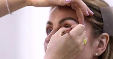 Makyöz, güzellik salonunda genç bir kadının profesyonel makyajını yapıyor.                