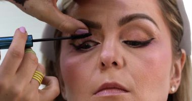 Makyöz, güzellik salonunda genç bir kadının profesyonel makyajını yapıyor.                