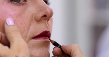 Güzellik salonundaki güzel kız modelin dudaklarına makyaj yapan profesyonel makyözün yakın plan görüntüsü.                 