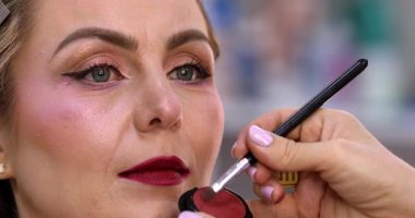 Makyöz, güzellik salonunda genç bir kadının profesyonel makyajını yapıyor.                