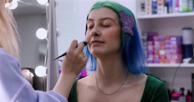 Parlak makyaj yapma süreci. Makyöz yüzüne makyaj yapan bir makyöz. Güzellik salonundaki genç yeşil saçlı kadının portresi..                        