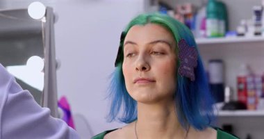 Parlak makyaj yapma süreci. Makyöz yüzüne makyaj yapan bir makyöz. Güzellik salonundaki genç yeşil saçlı kadının portresi..                        