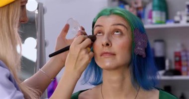 Parlak makyaj yapma süreci. Makyöz yüzüne makyaj yapan bir makyöz. Güzellik salonundaki genç yeşil saçlı kadının portresi..                        
