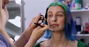 Parlak makyaj yapma süreci. Makyöz yüzüne makyaj yapan bir makyöz. Güzellik salonundaki genç yeşil saçlı kadının portresi..                        