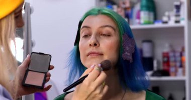 Parlak makyaj yapma süreci. Makyöz yüzüne makyaj yapan bir makyöz. Güzellik salonundaki genç yeşil saçlı kadının portresi..                        
