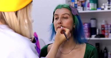 Parlak makyaj yapma süreci. Makyöz yüzüne makyaj yapan bir makyöz. Güzellik salonundaki genç yeşil saçlı kadının portresi..                        