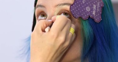 Parlak makyaj yapma süreci. Makyöz yüzüne makyaj yapan bir makyöz. Güzellik salonundaki genç yeşil saçlı kadının portresi..                        