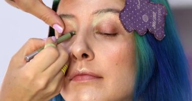 Parlak makyaj yapma süreci. Makyöz yüzüne makyaj yapan bir makyöz. Güzellik salonundaki genç yeşil saçlı kadının portresi..                        