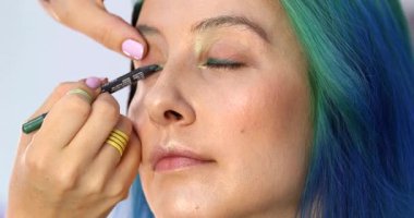 Parlak makyaj yapma süreci. Makyöz yüzüne makyaj yapan bir makyöz. Güzellik salonundaki genç yeşil saçlı kadının portresi..                        