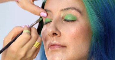 Parlak makyaj yapma süreci. Makyöz yüzüne makyaj yapan bir makyöz. Güzellik salonundaki genç yeşil saçlı kadının portresi..                        