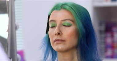 Parlak makyaj yapma süreci. Makyöz yüzüne makyaj yapan bir makyöz. Güzellik salonundaki genç yeşil saçlı kadının portresi..                        