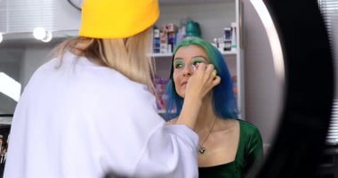 Parlak makyaj yapma süreci. Makyöz yüzüne makyaj yapan bir makyöz. Güzellik salonundaki genç yeşil saçlı kadının portresi..                        