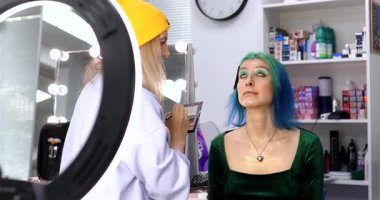 Parlak makyaj yapma süreci. Makyöz yüzüne makyaj yapan bir makyöz. Güzellik salonundaki genç yeşil saçlı kadının portresi..                        