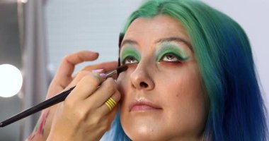 Parlak makyaj yapma süreci. Makyöz yüzüne makyaj yapan bir makyöz. Güzellik salonundaki genç yeşil saçlı kadının portresi..                        