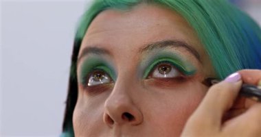 Parlak makyaj yapma süreci. Makyöz yüzüne makyaj yapan bir makyöz. Güzellik salonundaki genç yeşil saçlı kadının portresi..                        