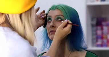 Parlak makyaj yapma süreci. Makyöz yüzüne makyaj yapan bir makyöz. Güzellik salonundaki genç yeşil saçlı kadının portresi..                        