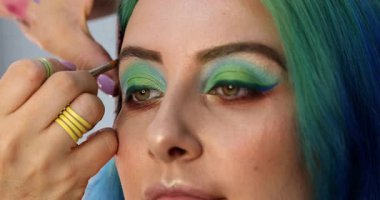 Parlak makyaj yapma süreci. Makyöz yüzüne makyaj yapan bir makyöz. Güzellik salonundaki genç yeşil saçlı kadının portresi..                        