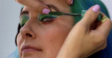 Parlak makyaj yapma süreci. Makyöz yüzüne makyaj yapan bir makyöz. Güzellik salonundaki genç yeşil saçlı kadının portresi..                        