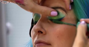 Parlak makyaj yapma süreci. Makyöz yüzüne makyaj yapan bir makyöz. Güzellik salonundaki genç yeşil saçlı kadının portresi..                        