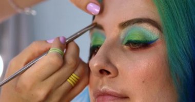Parlak makyaj yapma süreci. Makyöz yüzüne makyaj yapan bir makyöz. Güzellik salonundaki genç yeşil saçlı kadının portresi..                        