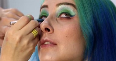 Parlak makyaj yapma süreci. Makyöz yüzüne makyaj yapan bir makyöz. Güzellik salonundaki genç yeşil saçlı kadının portresi..                        
