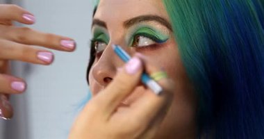 Parlak makyaj yapma süreci. Makyöz yüzüne makyaj yapan bir makyöz. Güzellik salonundaki genç yeşil saçlı kadının portresi..                        