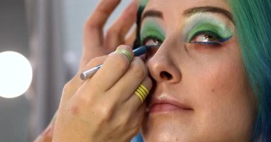 Parlak makyaj yapma süreci. Makyöz yüzüne makyaj yapan bir makyöz. Güzellik salonundaki genç yeşil saçlı kadının portresi..                        