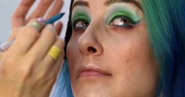 Parlak makyaj yapma süreci. Makyöz yüzüne makyaj yapan bir makyöz. Güzellik salonundaki genç yeşil saçlı kadının portresi..                        