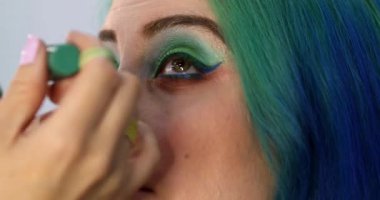 Parlak makyaj yapma süreci. Makyöz yüzüne makyaj yapan bir makyöz. Güzellik salonundaki genç yeşil saçlı kadının portresi..                        