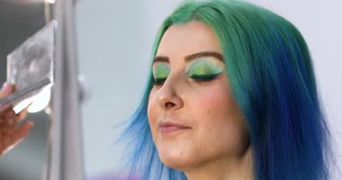 Parlak makyaj yapma süreci. Makyöz yüzüne makyaj yapan bir makyöz. Güzellik salonundaki genç yeşil saçlı kadının portresi..                        