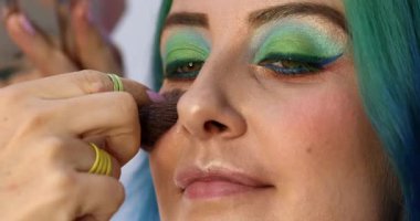 Parlak makyaj yapma süreci. Makyöz yüzüne makyaj yapan bir makyöz. Güzellik salonundaki genç yeşil saçlı kadının portresi..                        