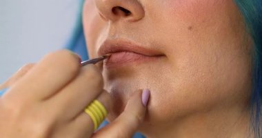 Güzellik salonundaki güzel kız modelin dudaklarına makyaj yapan profesyonel makyözün yakın plan görüntüsü.                 