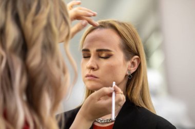 Makyaj sanatçısı genç ve güzel bir kadınla profesyonel makyaj yapıyor..        