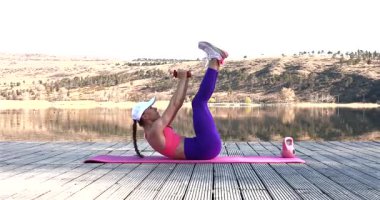 Göl kenarında spor yapan genç bir kadın. Kadın fitness eğitmeni ahşap nehir salında dışarıda egzersiz yapıyor.